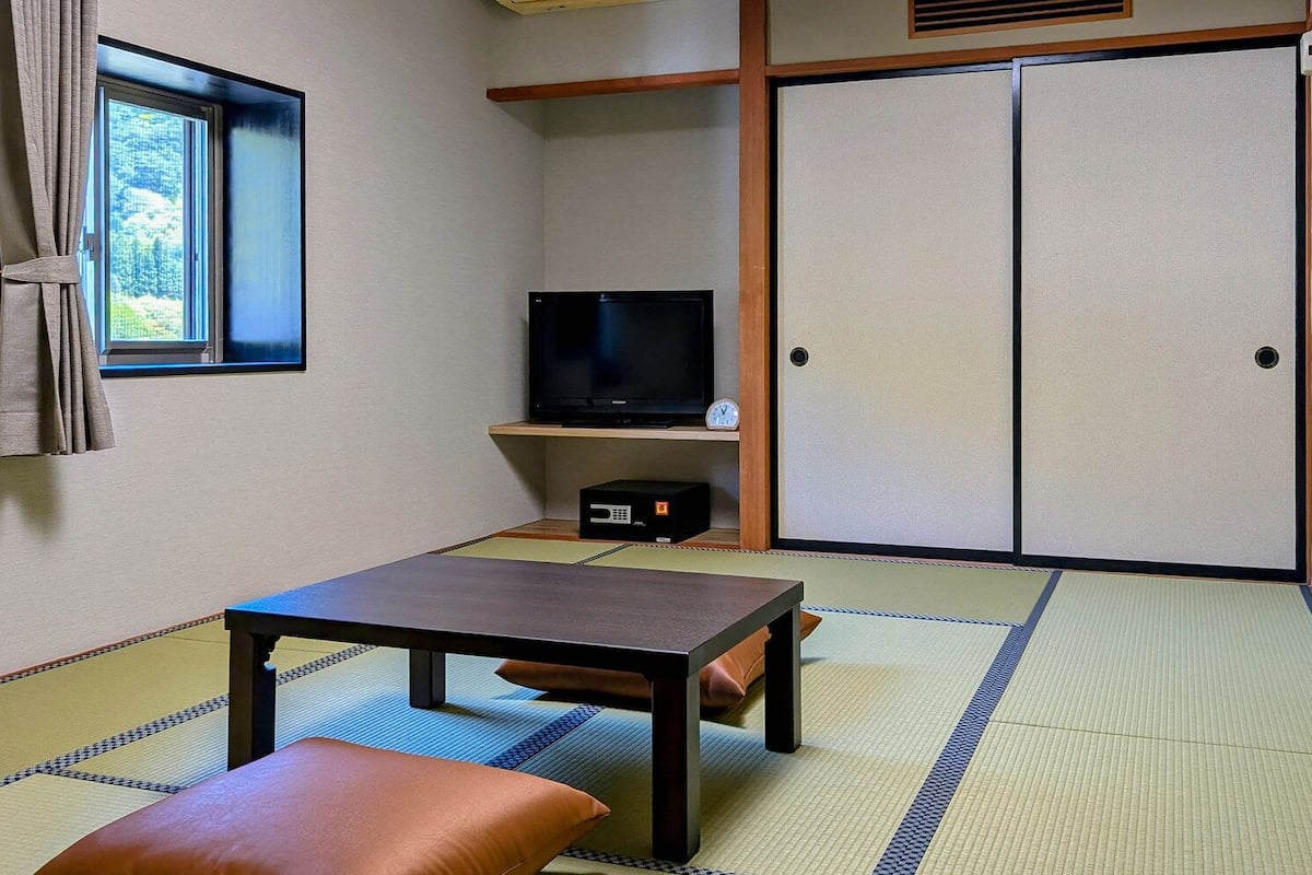 Ett traditionellt japanskt rum med tatamimattor på golvet, ett lågt bord, en bänk, en tv och skjutdörrar.