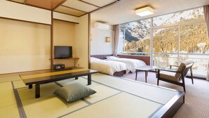 Una habitación tradicional japonesa con suelo de tatami, televisor, dos camas, una mesita y una silla.