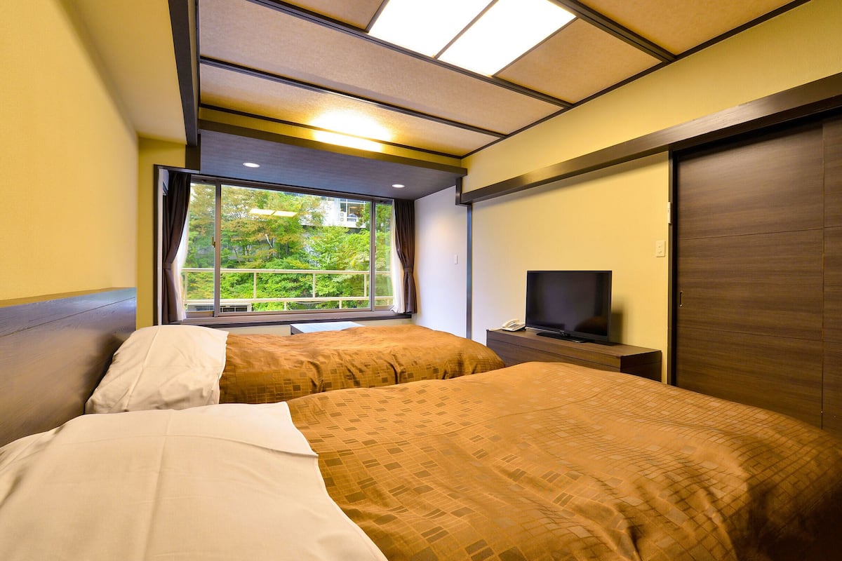 Ett hotellrum med två sängar, en tv och ett fönster med utsikt över grönområden.