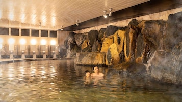 An indoor hot spring area with a rocky wall and multiple benches.