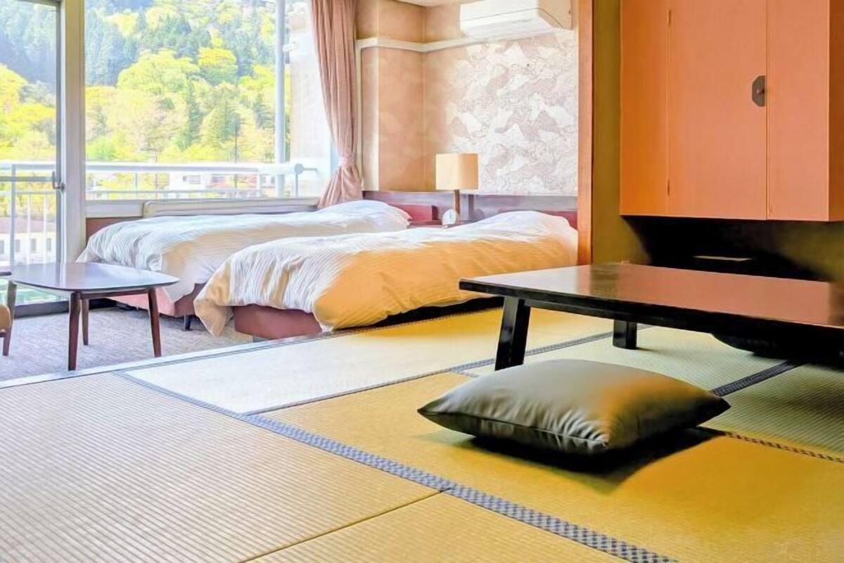 Ett hotellrum med två sängar, en TV, ett bord och utsikt över träd.