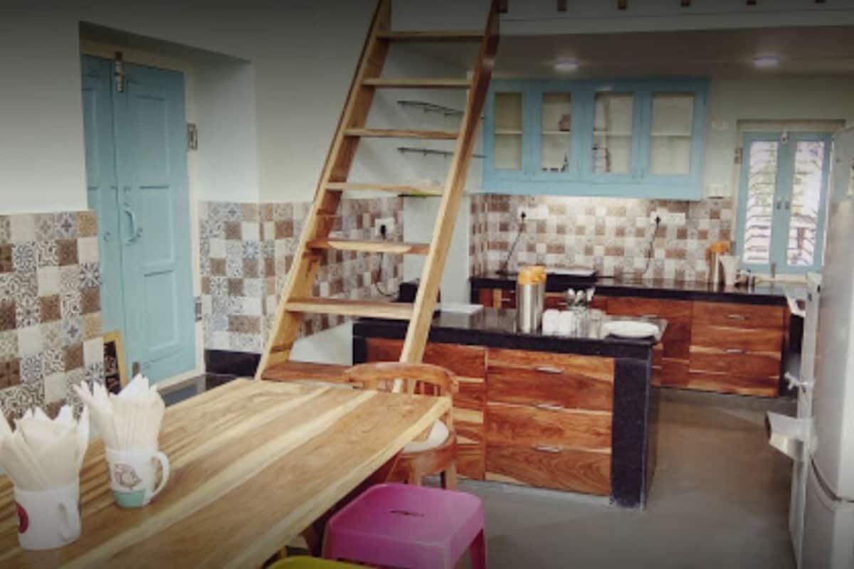 Una cocina con una mesa de madera, un taburete rosa, una escalera y un refrigerador.