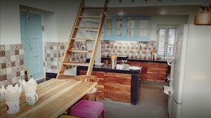 A kitchen with a wooden table, a pink stool, a ladder, and a refrigerator. - Jaipur Jantar Hostel (Jaipur)