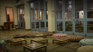 A room with a wooden floor, multiple round ottomans, and a large window with blue shutters. - Jaipur Jantar Hostel (Jaipur)