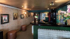 A bar area with a brick wall, framed posters, a counter with a green mat, and a neon sign. - My Hotel Herrity (Bangkok)