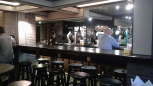 A bar area with stools and tables, a counter with staff, and a brick wall. - My Hotel Herrity (Bangkok)