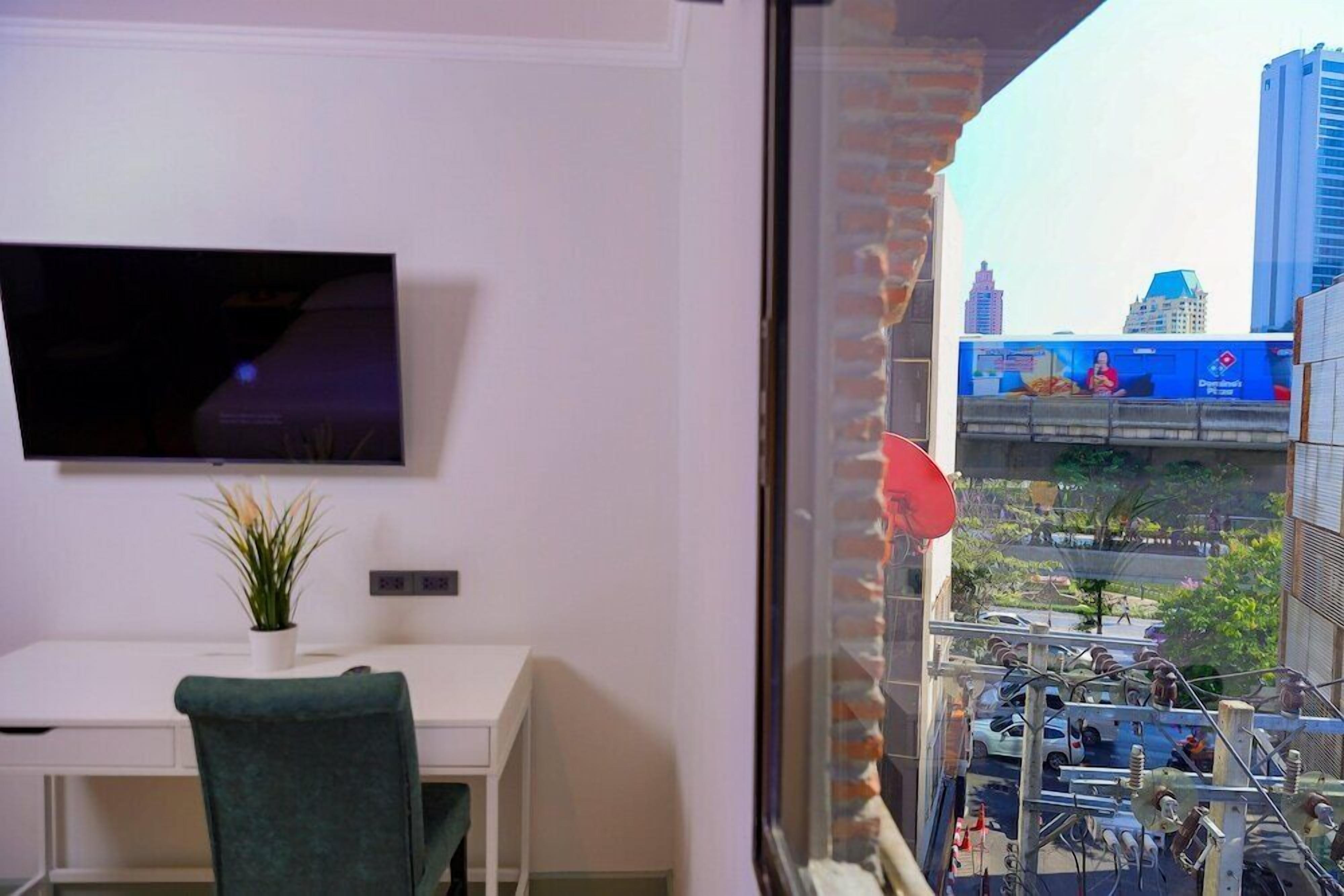 A room with a desk, a television, and a window overlooking a cityscape.