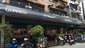 A building with a Guinness and O'Shea's sign, a motorcycle parked in front, and a weekly specials menu board. - My Hotel Herrity (Bangkok)