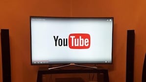 Un téléviseur affichant le logo de YouTube, posé sur un support en bois dans une pièce dont le sol est également en bois.