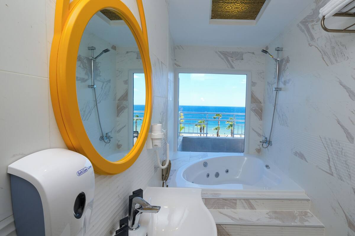 A bathroom with a large mirror, a bathtub, and a view of the ocean.