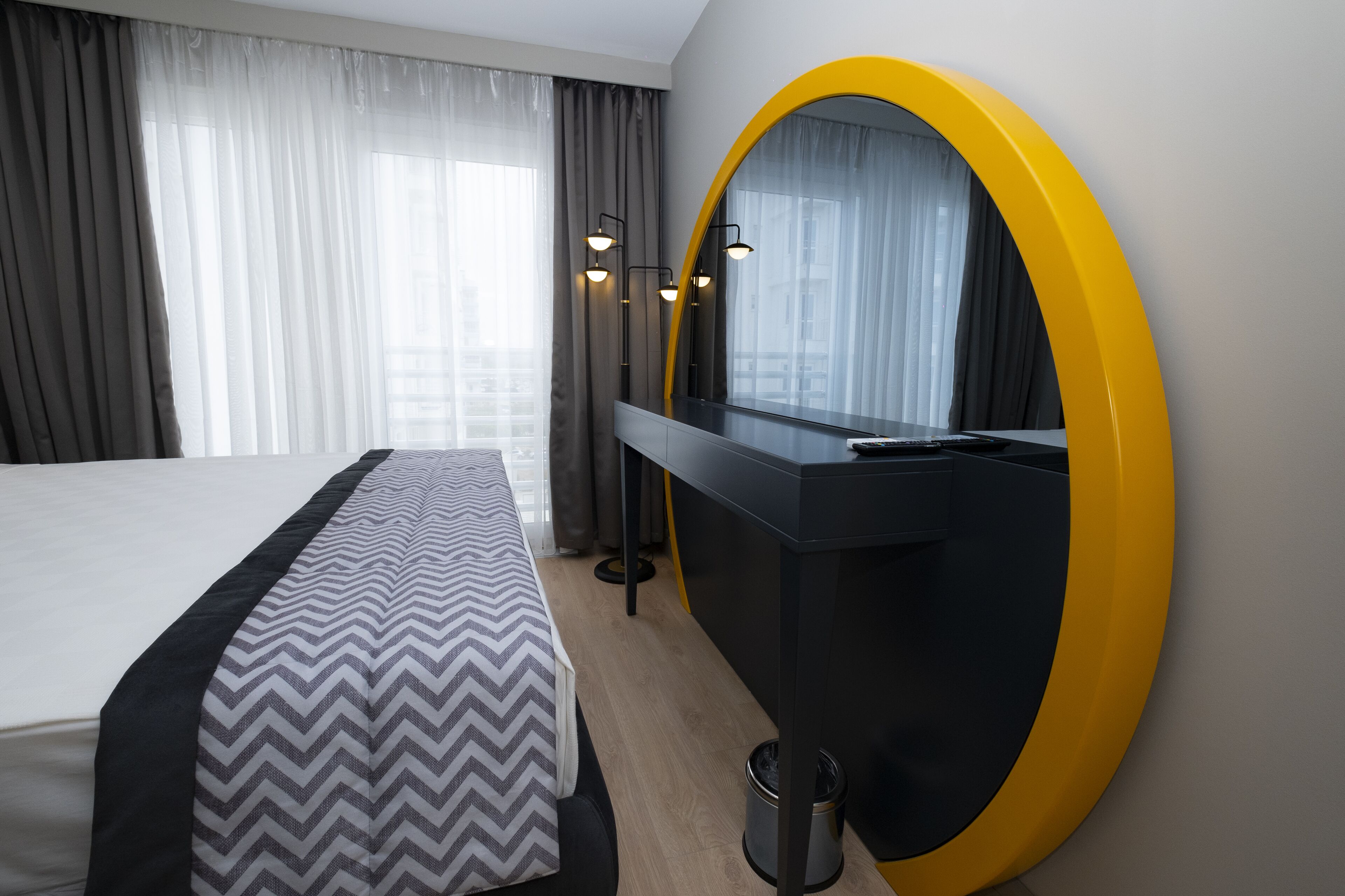 A hotel room with a bed, a desk, a mirror, and a window with curtains.