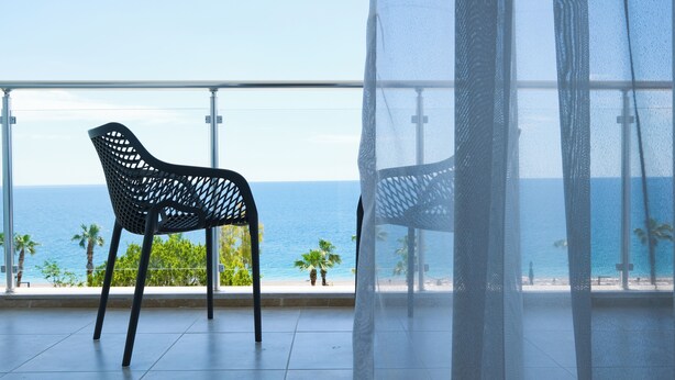 A balcony with a mesh screen, a black chair, and a view of the ocean. - Sea City Devran Hotel & Spa (Konyaalti)