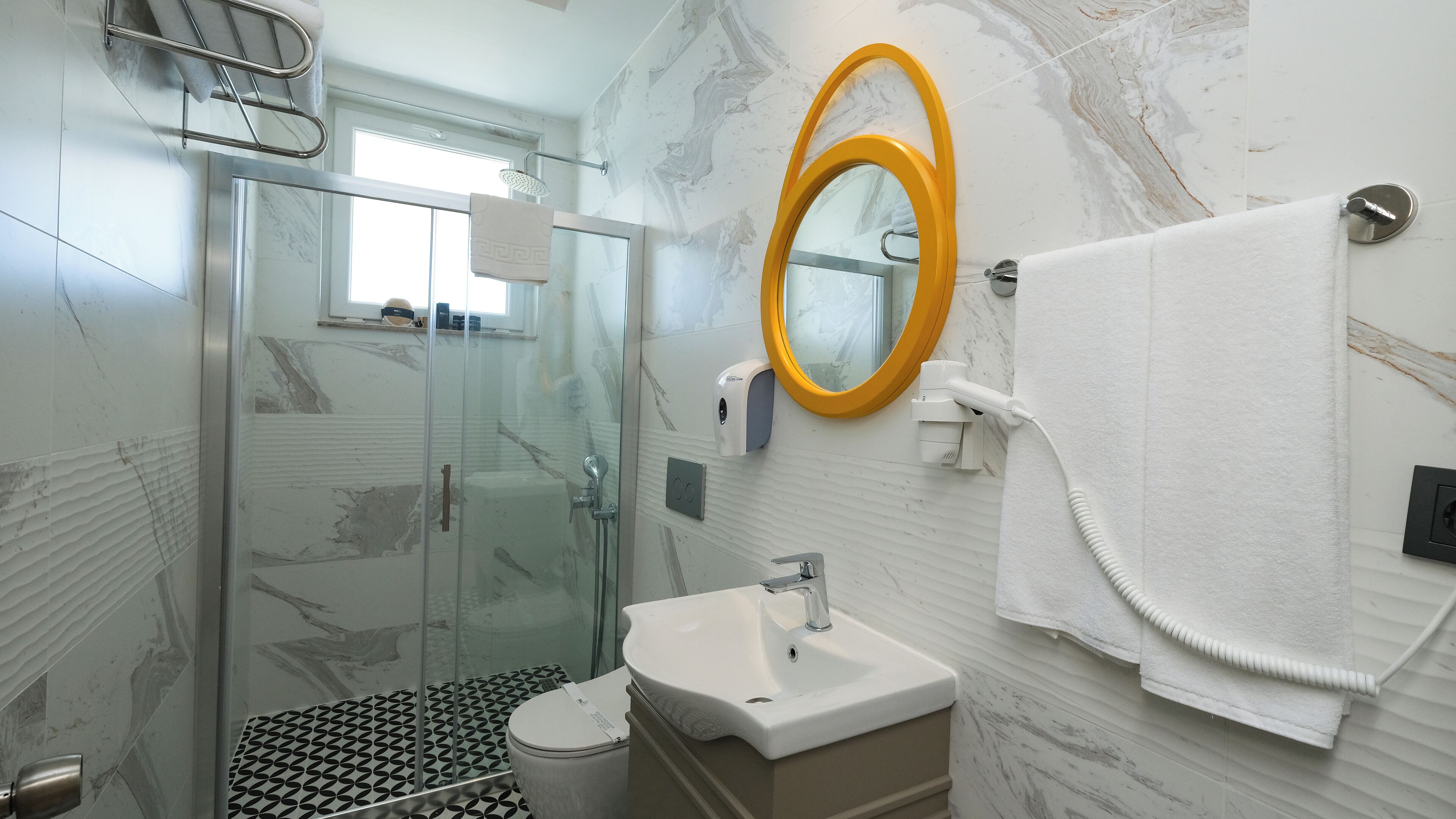 Un baño con cabina de ducha de vidrio, un lavabo, un espejo y un perchero para toallas.