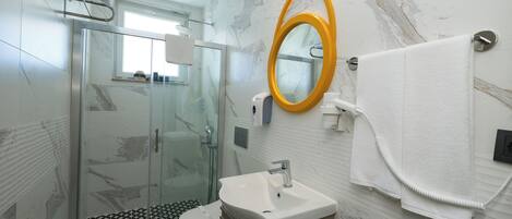 Un baño con cabina de ducha de vidrio, un lavabo, un espejo y un perchero para toallas.