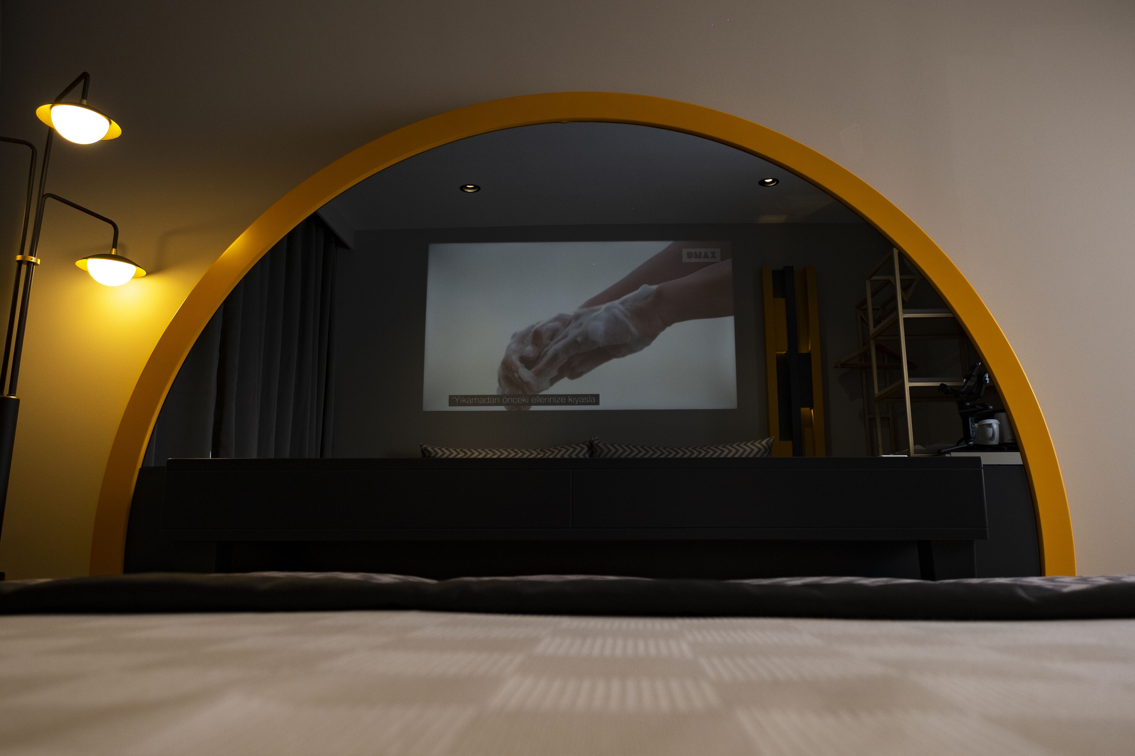 Un dormitorio con una cama, un televisor montado en una pared curva y un escritorio con una silla.