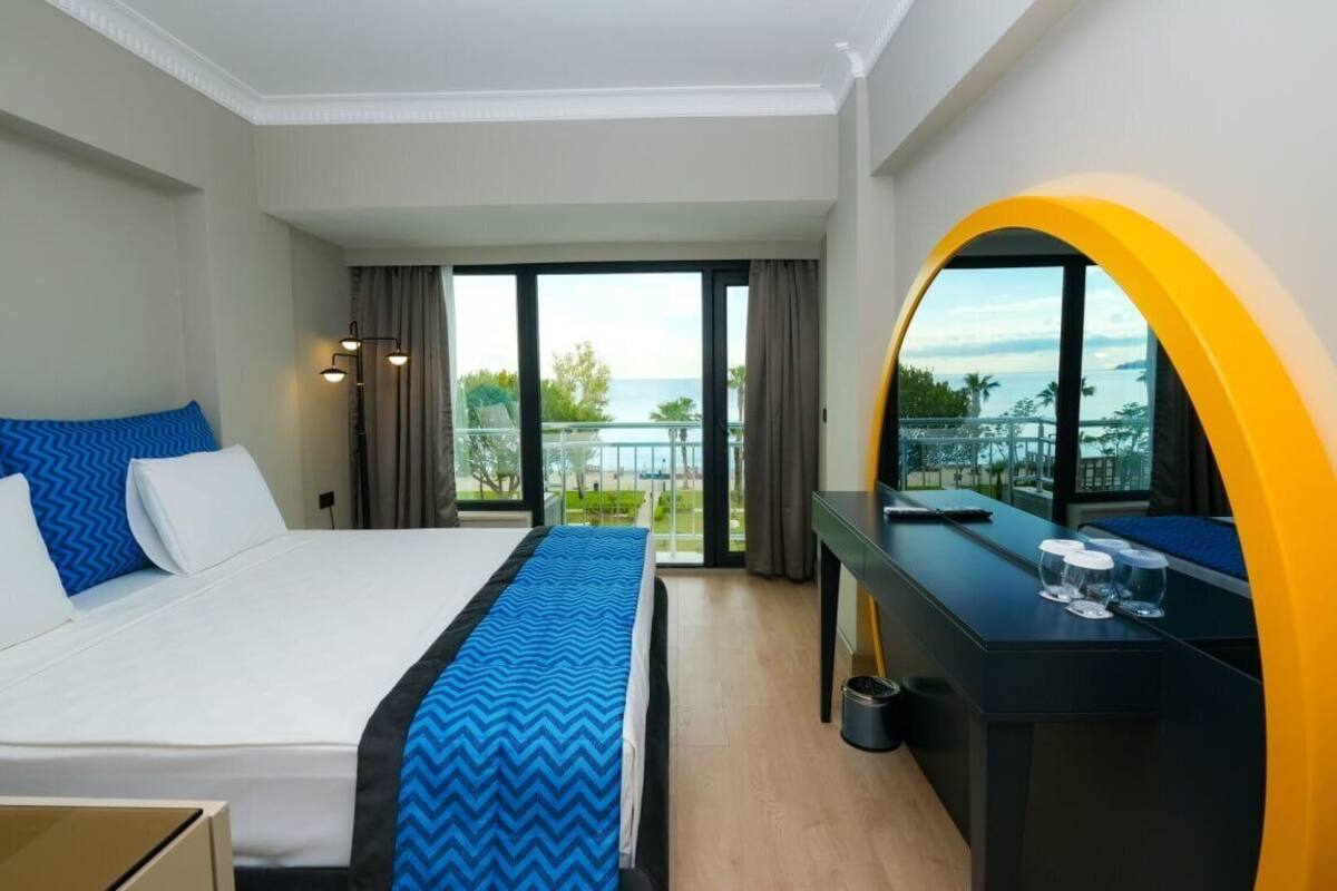 A hotel room with a bed, a desk, a view of the sea, and a balcony.