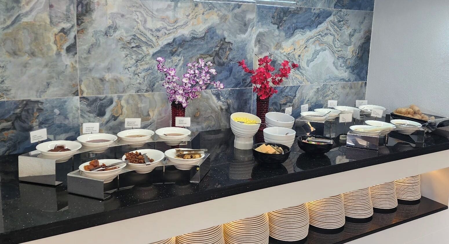 A buffet setup with various food items and a marble wall in the background.