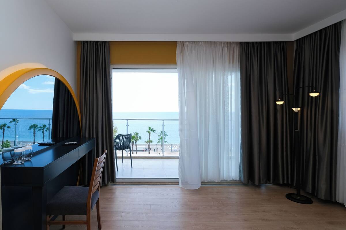 A modern hotel room with a balcony, a desk with a chair, and a view of the sea.