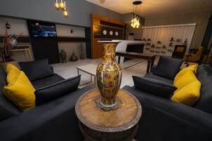 Una sala de estar moderna con un gran jarrón decorativo sobre una mesa de madera, sofás negros con cojines amarillos y un televisor montado en la pared.