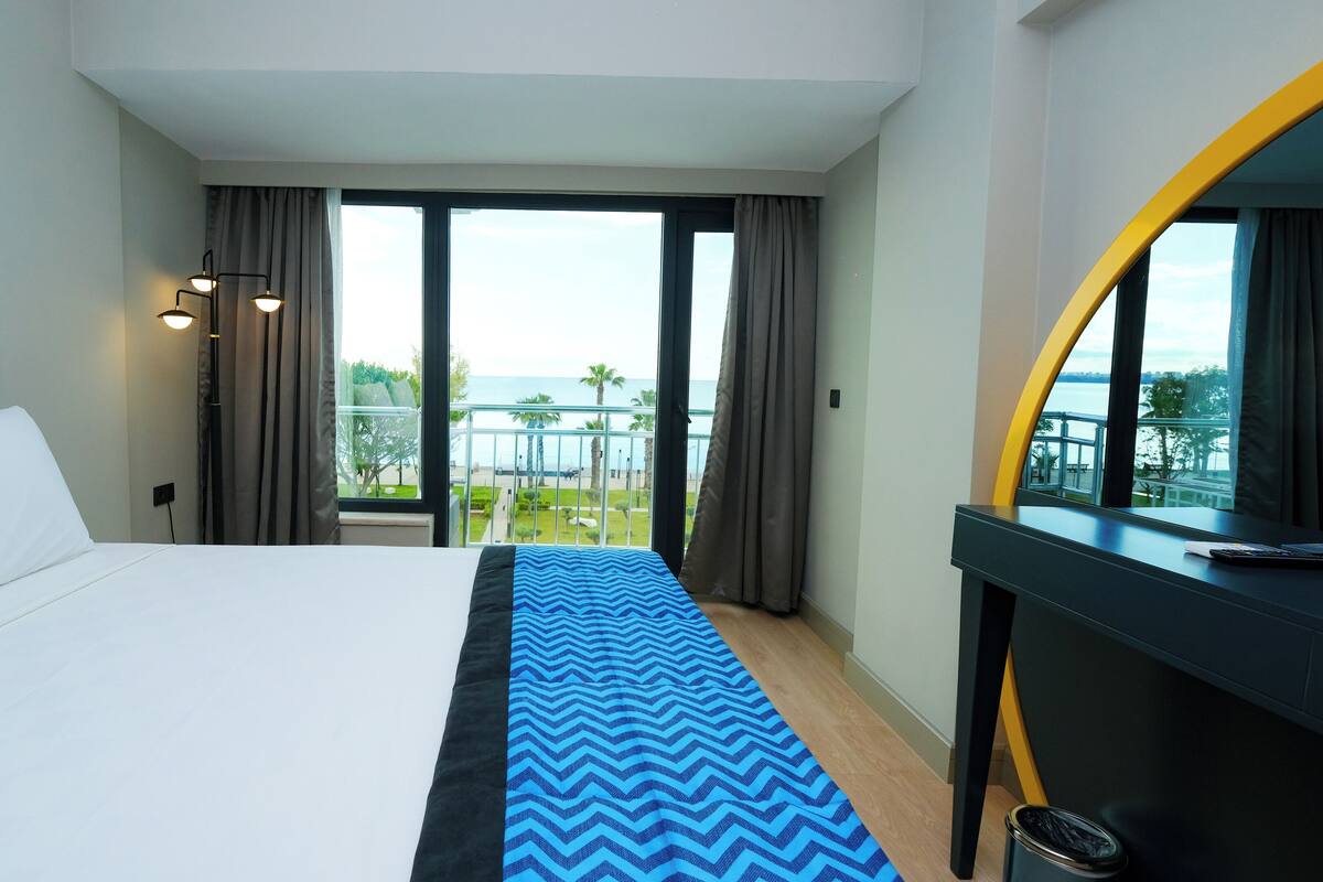 A hotel room with a bed, a desk, and a view of the sea.