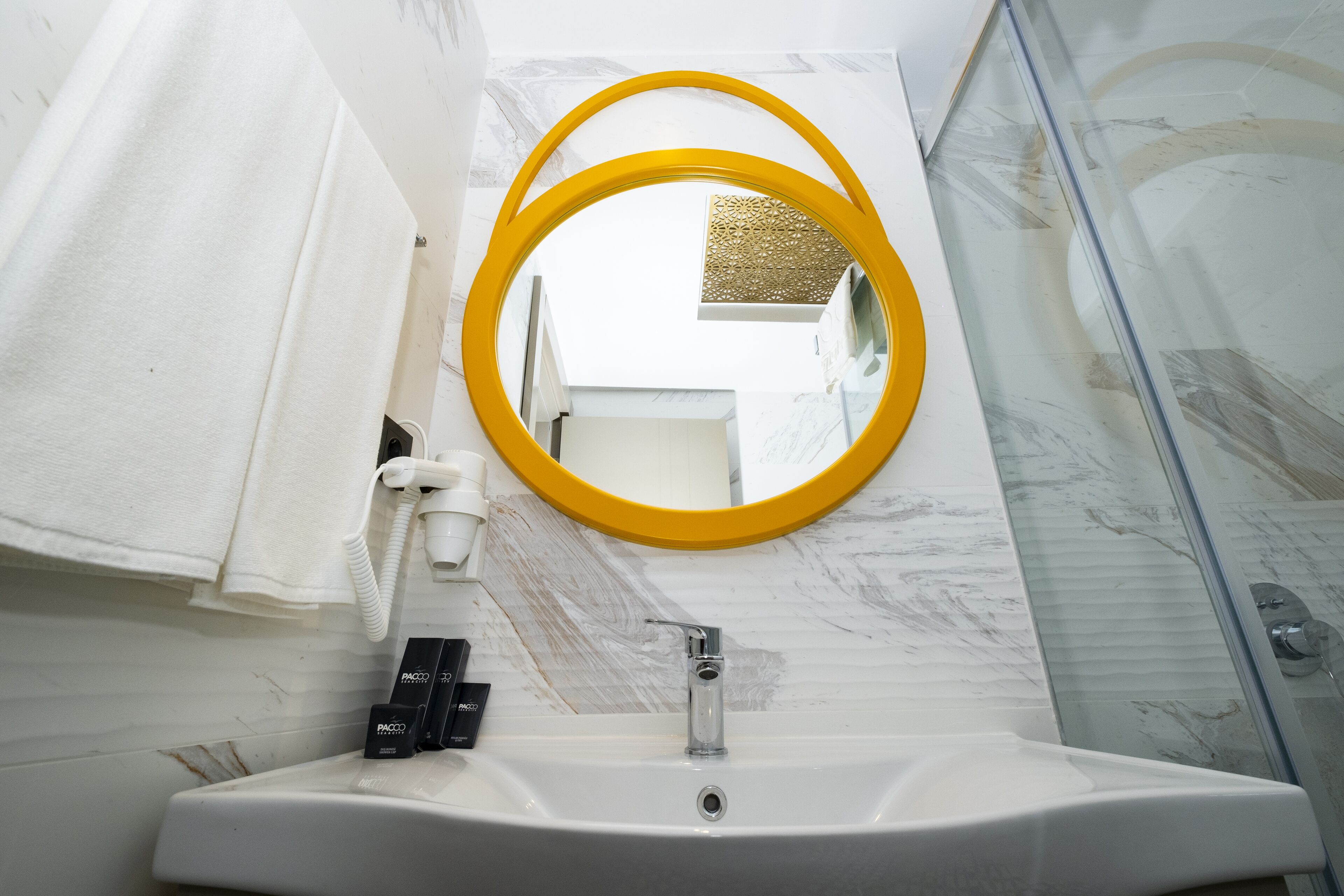Ein Badezimmer mit einem weißen Waschbecken, einem spiegel mit gelbem Rahmen und einer Glasdusche.