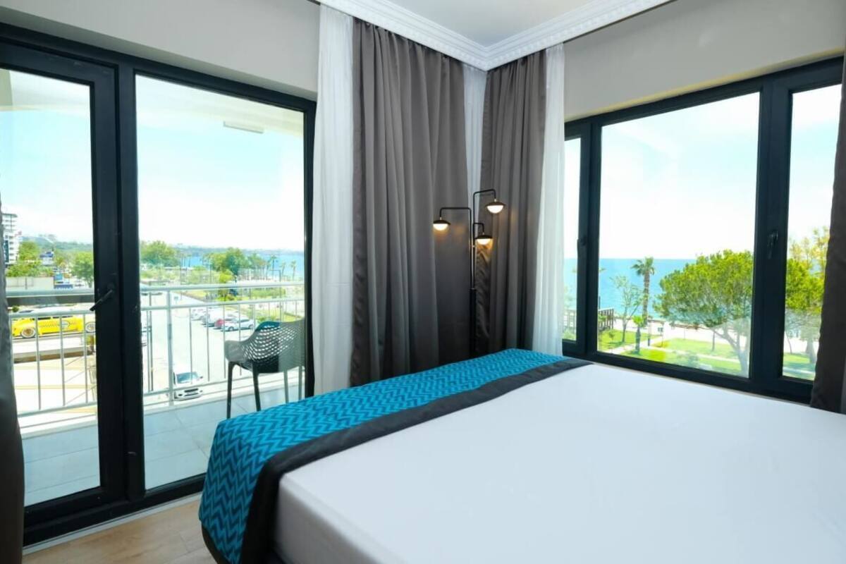A hotel room with a large bed, a balcony with a chair, and a view of the city.