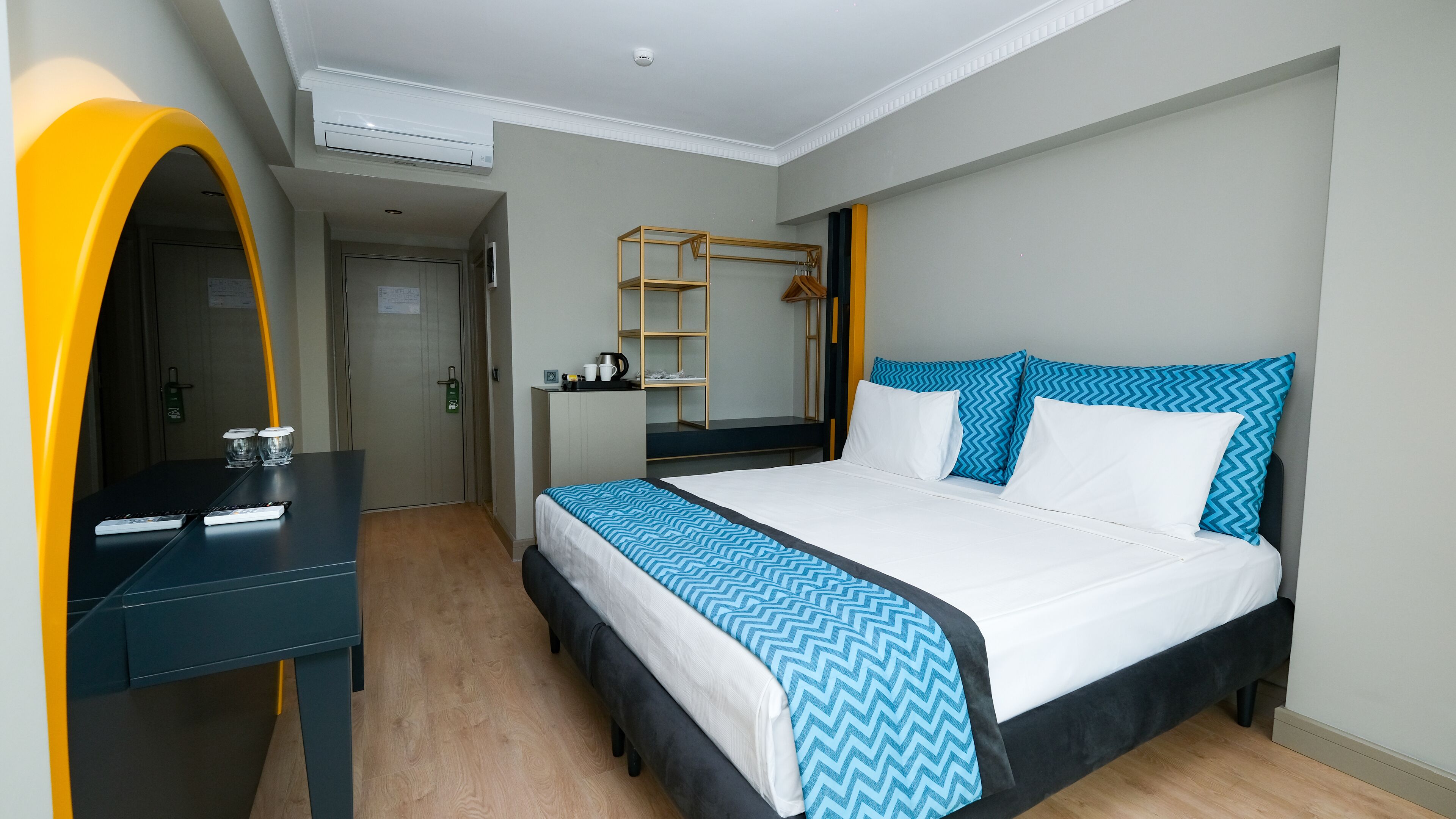 A hotel room with a bed, a desk, a mirror, a wardrobe, and a shelf with toiletries.