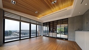 A spacious room with large windows, a wooden floor, and a modern ceiling design.