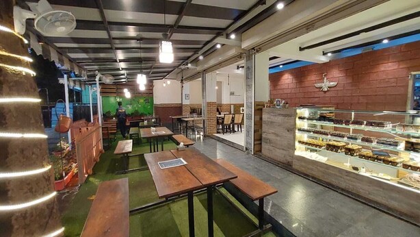 Un café con mesas y sillas de madera, una vitrina con productos de repostería y una pared de ladrillo.