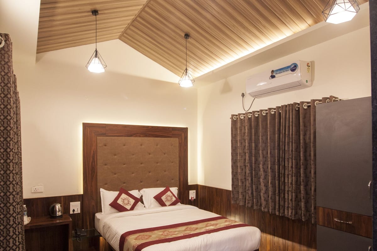 Habitación de hotel con techo de madera, una cama grande con cabecera, mesitas de noche, un armario y una unidad de aire acondicionado instalada en el techo.