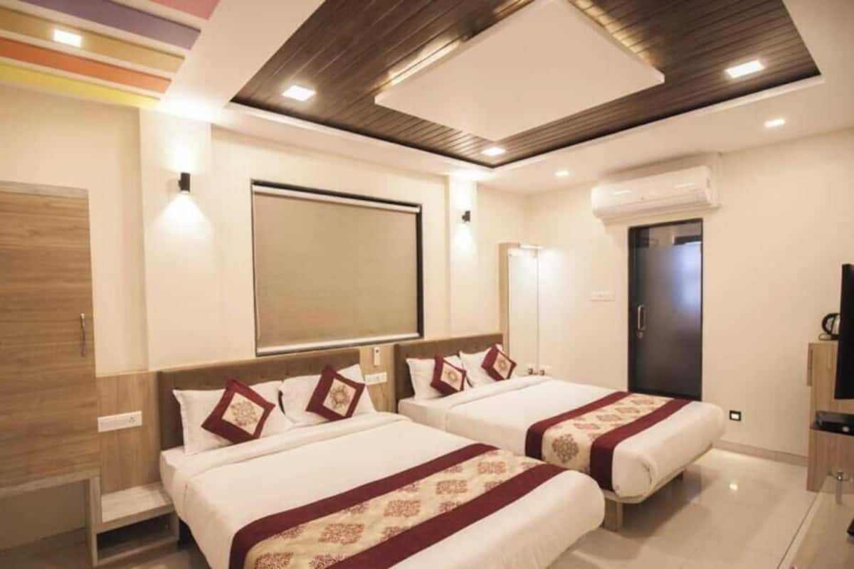 Una habitación de hotel con dos camas, un espejo grande, un equipo de aire acondicionado y un televisor.