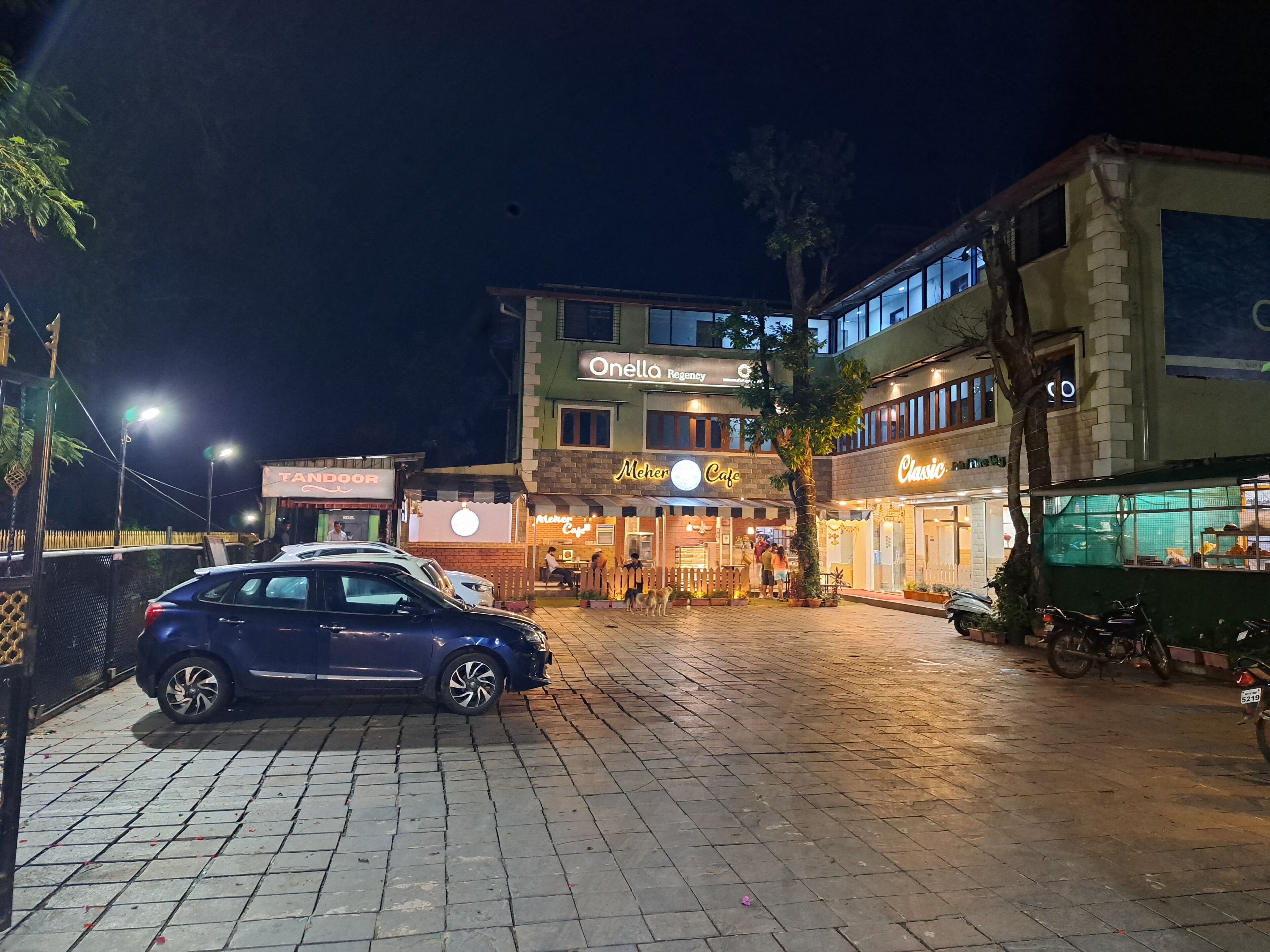 A nighttime street scene with a blue car parked on the side.
