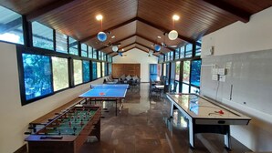 Un espacio interior amplio con mesa de futbolín, mesa de ping pong y generosas ventanas que dejan entrar luz natural y ofrecen vistas al exterior.