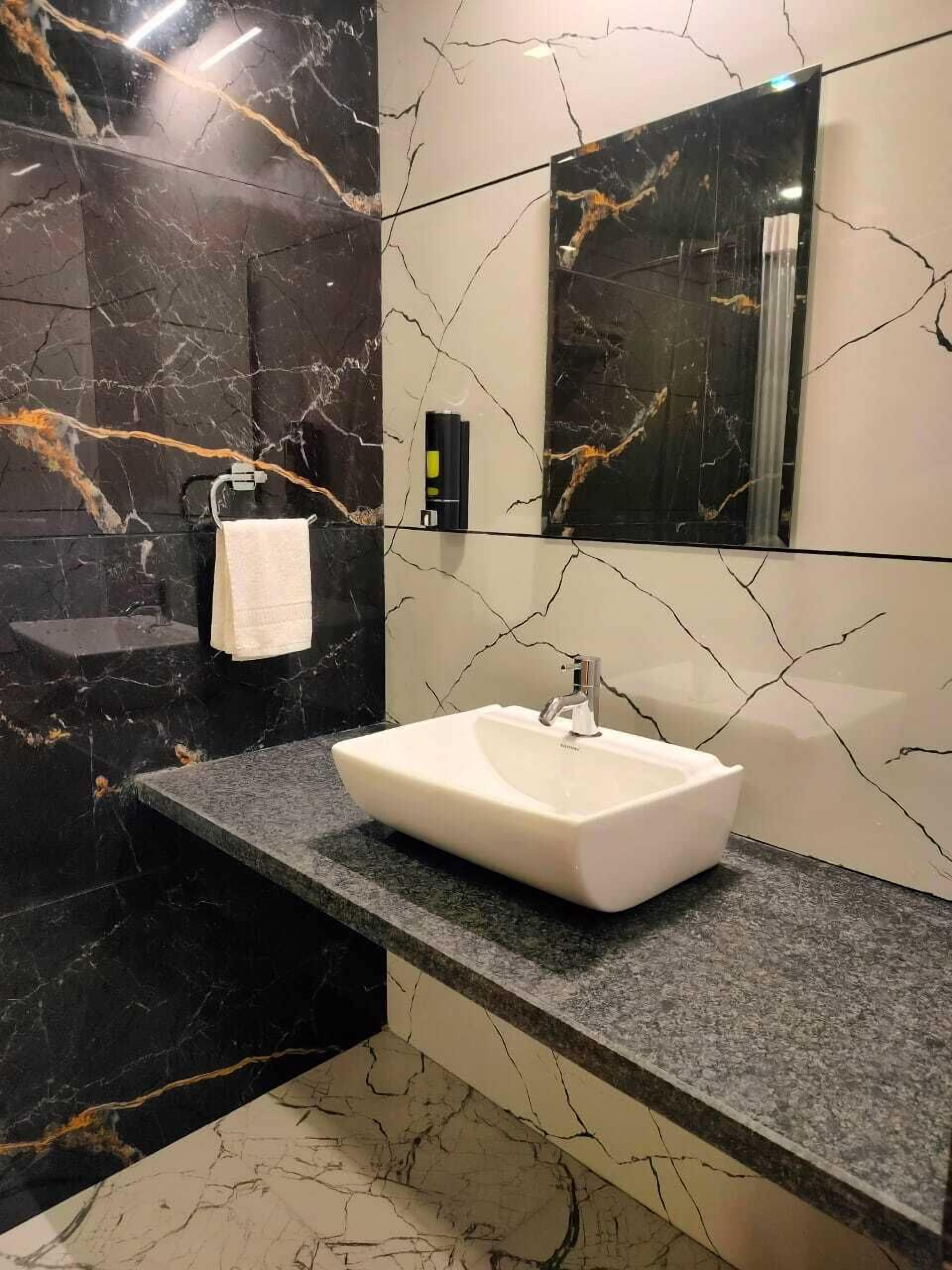 Une salle de bain moderne avec un lavabo blanc, des murs en marbre noir et un grand miroir.