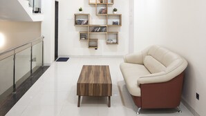 Una sala de estar moderna con una escalera, una mesa de centro de madera, un sofá color crema y estantes empotrados con libros y objetos decorativos.