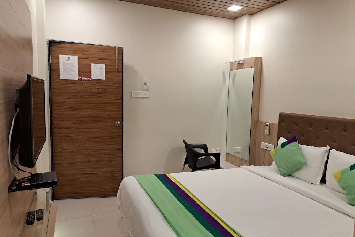 Habitación de hotel con cama, televisor, escritorio con computadora y puerta con letrero de 'No Fumar'.