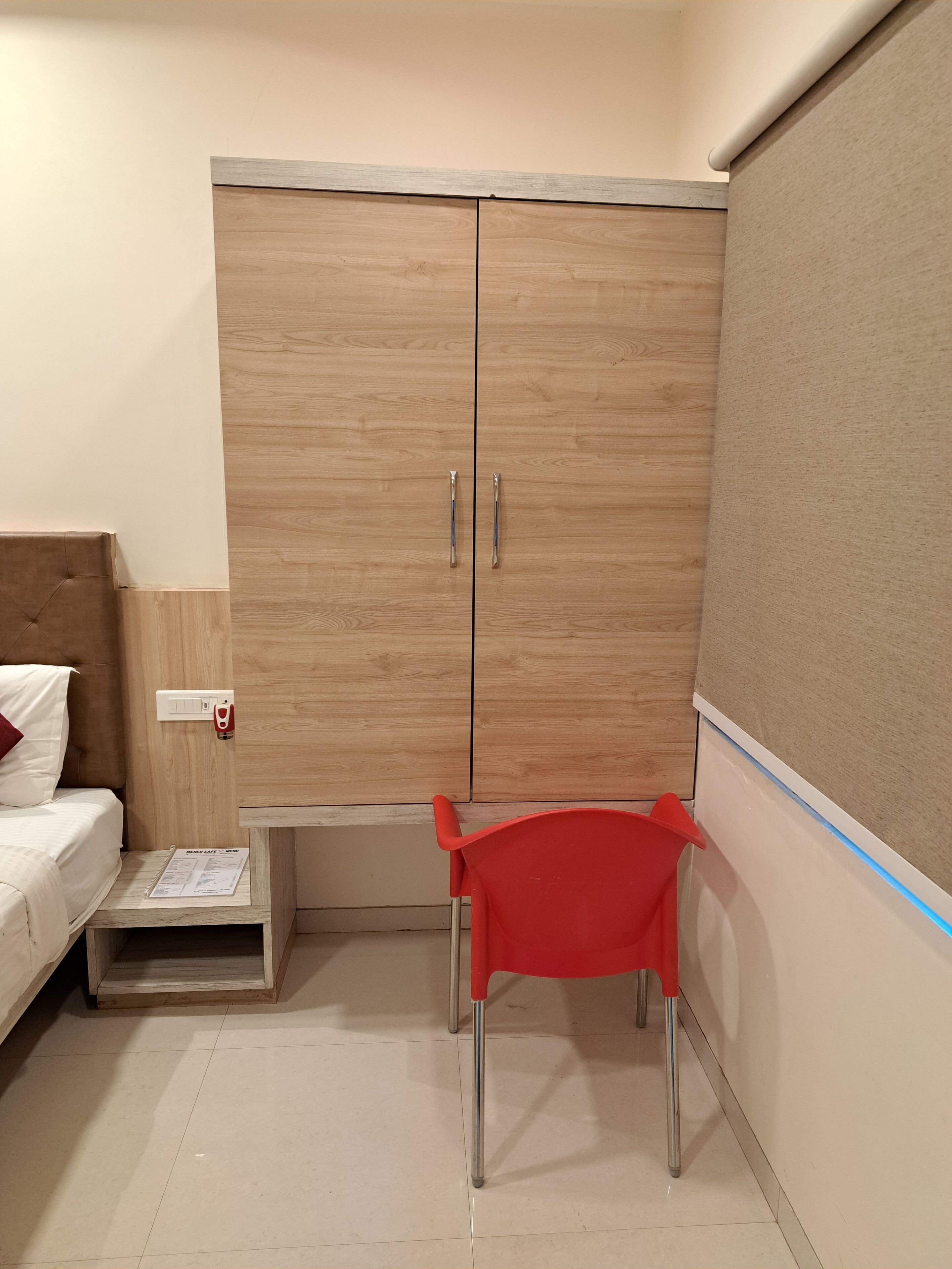 Un dormitorio con un armario de madera, una cama con cabecera, una silla roja y una mesita con un menú.