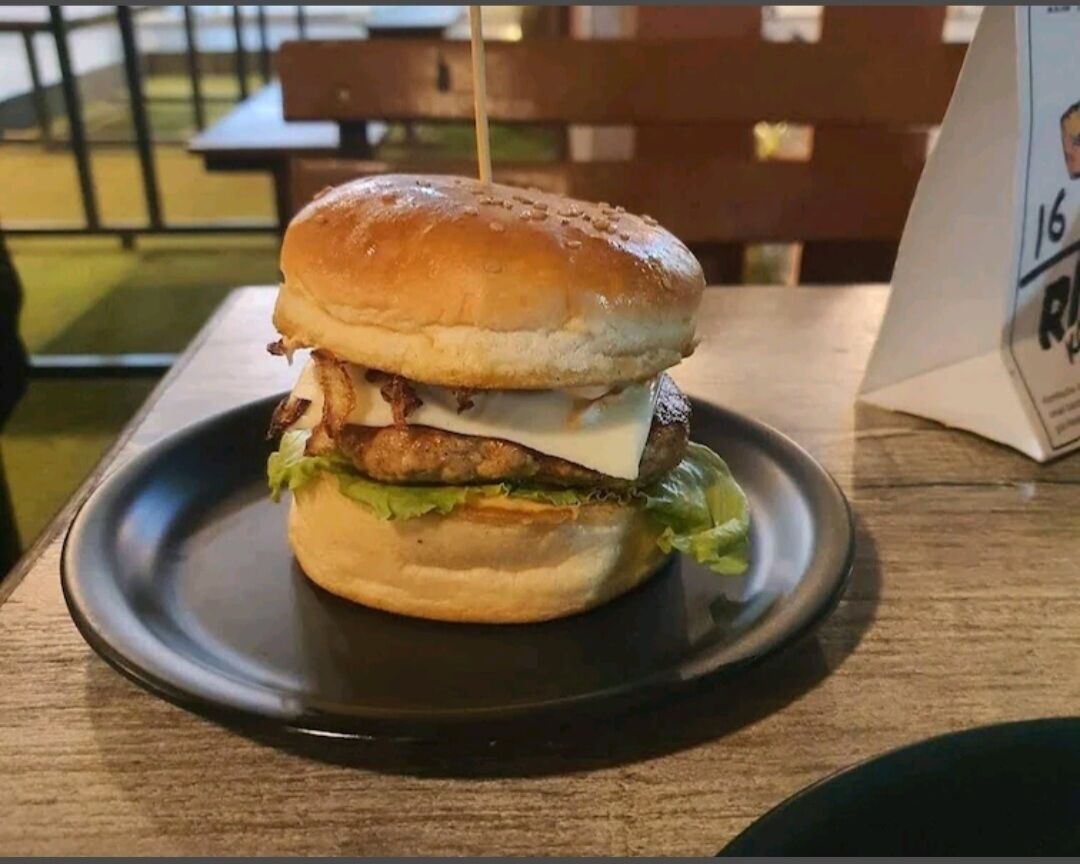 A burger on a black plate with a wooden table and a bench in the background.