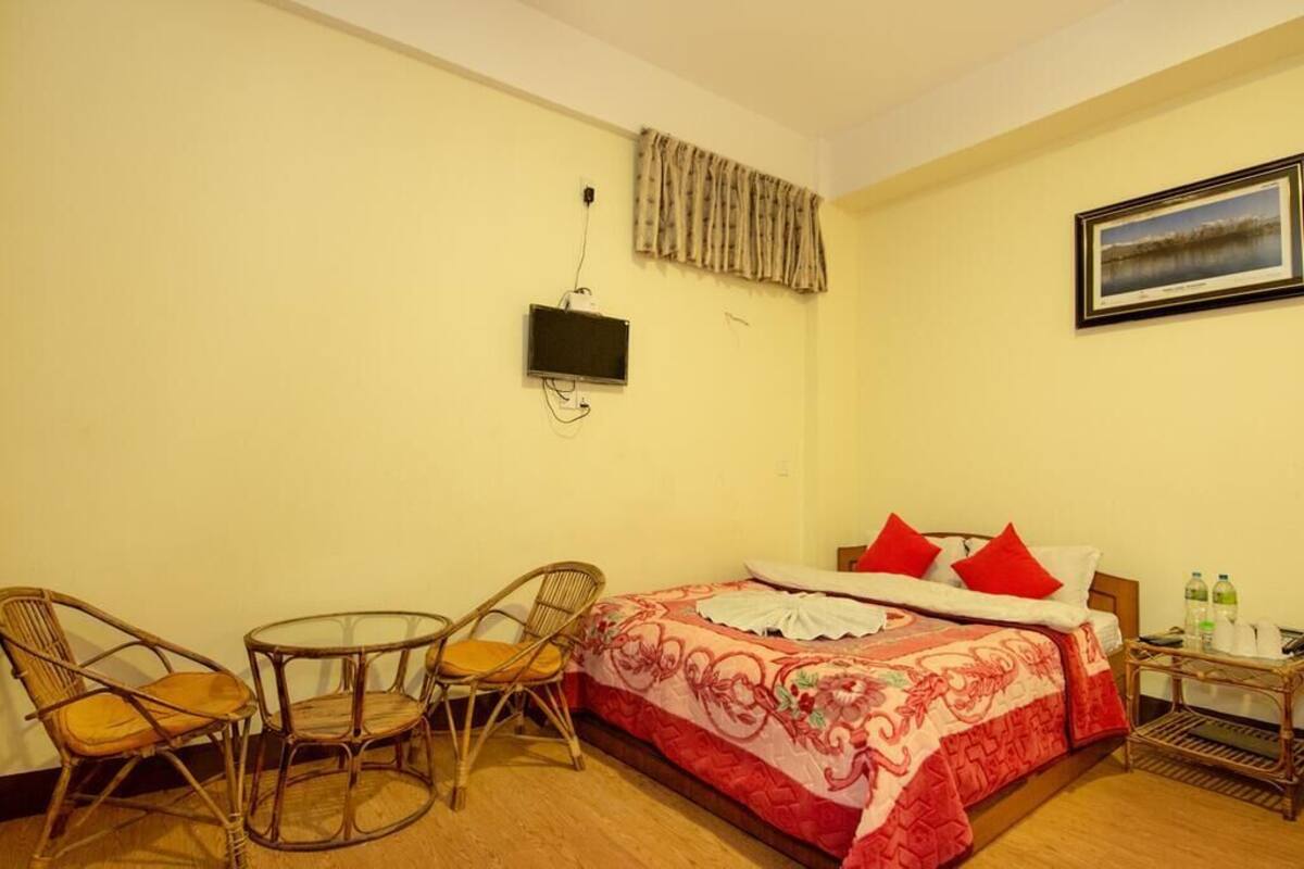 Una habitación con una cama, dos sillones de mimbre, una mesita, un televisor y un cuadro en la pared.