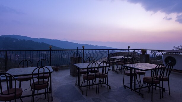 An outdoor terrace with tables and chairs, overlooking a mountainous landscape. - Hotel Marigold (Mahamanjushree Nagarkot)