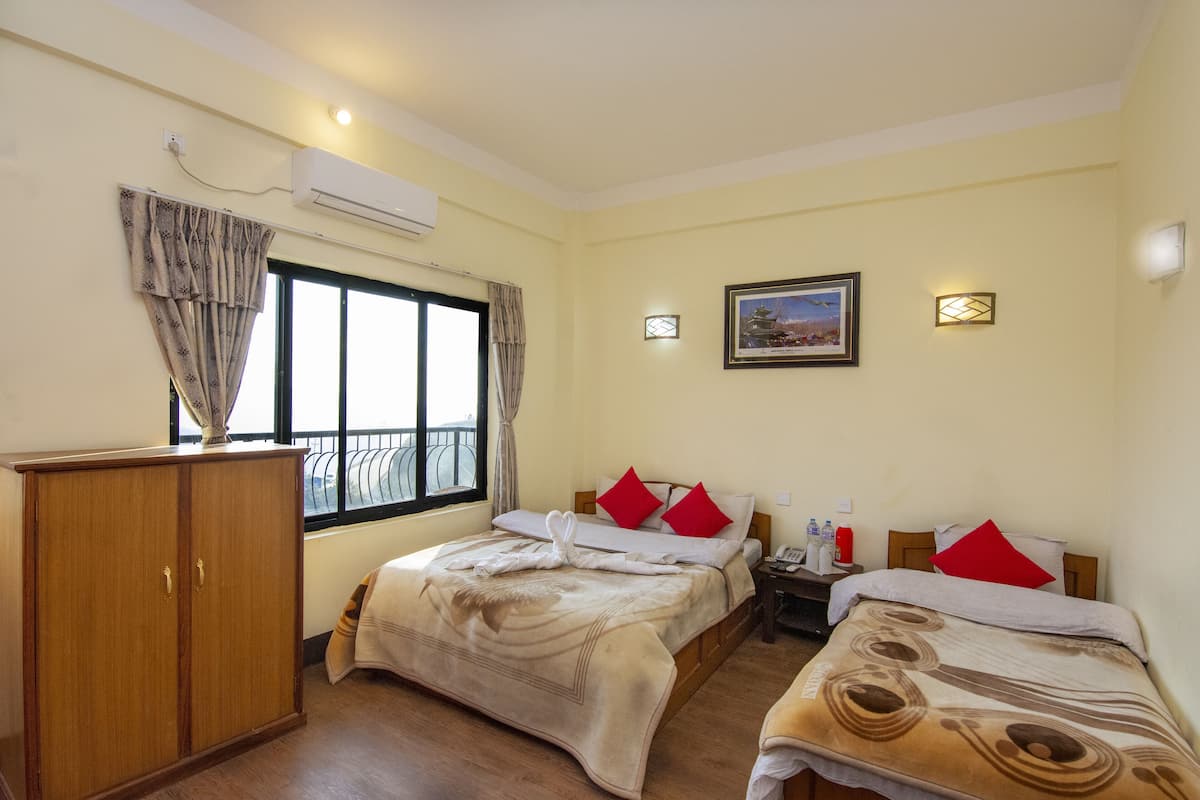 Habitación de hotel con dos camas, un armario, una ventana con cortinas, aire acondicionado instalado en la pared, una mesita de noche con teléfono y un cuadro enmarcado en la pared.