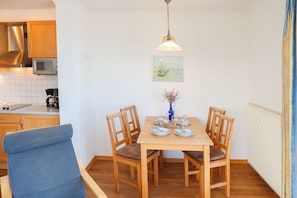 A dining area with a wooden table set for four, surrounded by wooden chairs. A blue upholstered chair is positioned in front of the table.