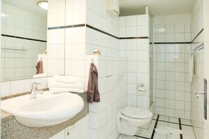 Un baño con lavamanos, espejo, inodoro y ducha.