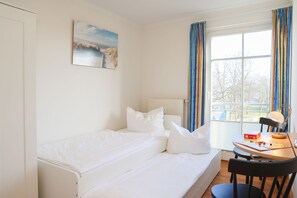 Una habitación con una cama, una mesa con una lámpara y un ventanal con cortinas.