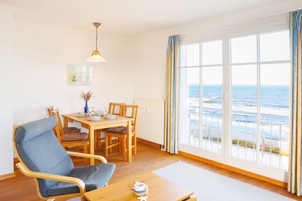 A room with a view of the ocean, a dining table with chairs, a blue chair, and a hanging light fixture.