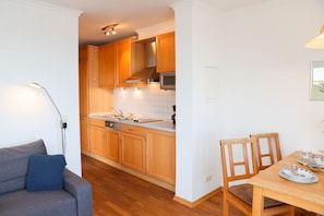 A modern kitchen with wooden cabinets, a built-in oven, and a dining area with a table and chairs.