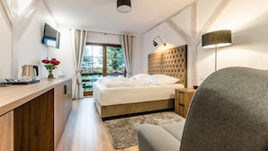 Une chambre moderne avec un lit, une table de chevet, une lampe et une vue sur la verdure à l’extérieur.