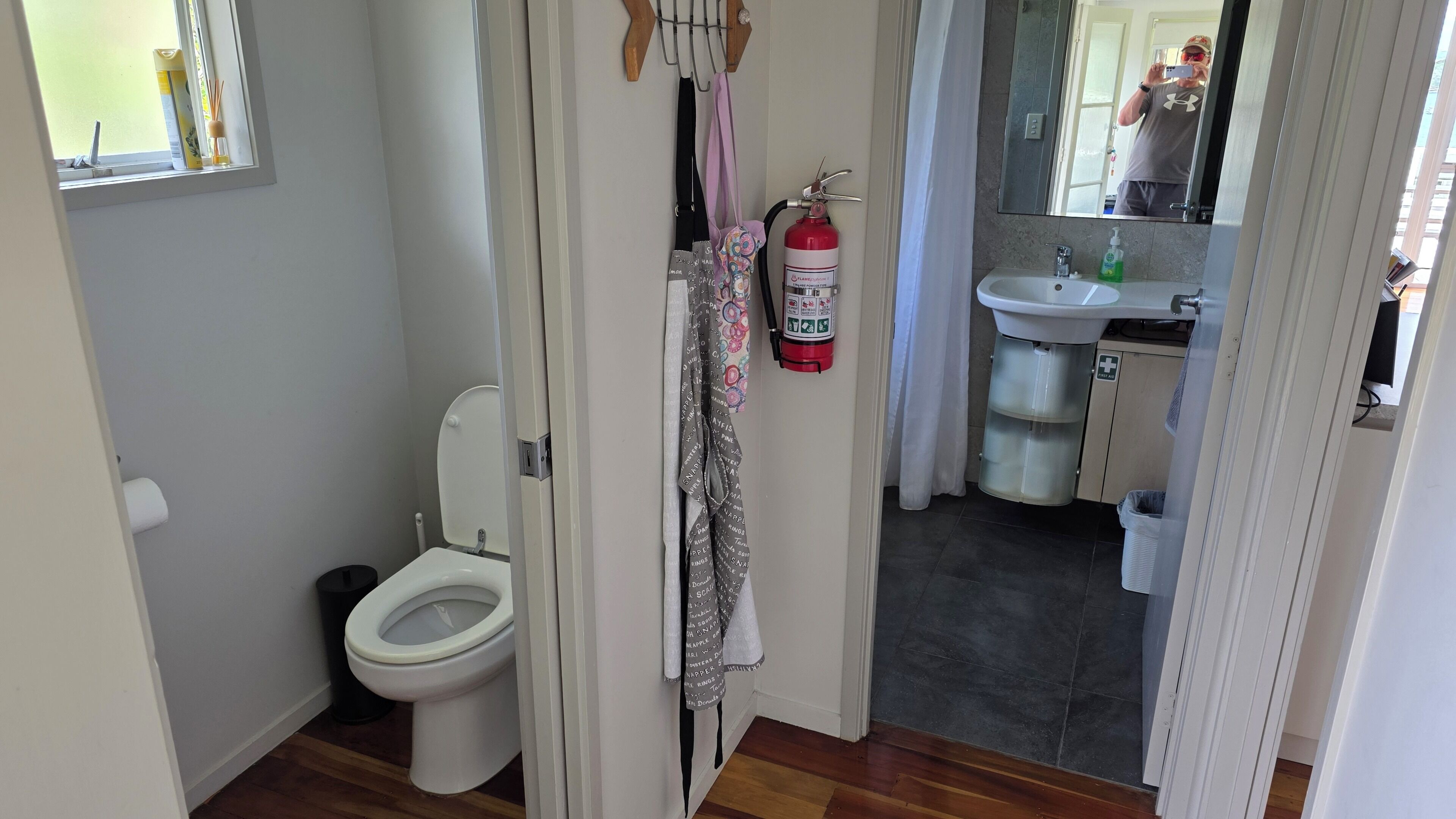 Un bagno con il water, un estintore, un lavandino e uno specchio.