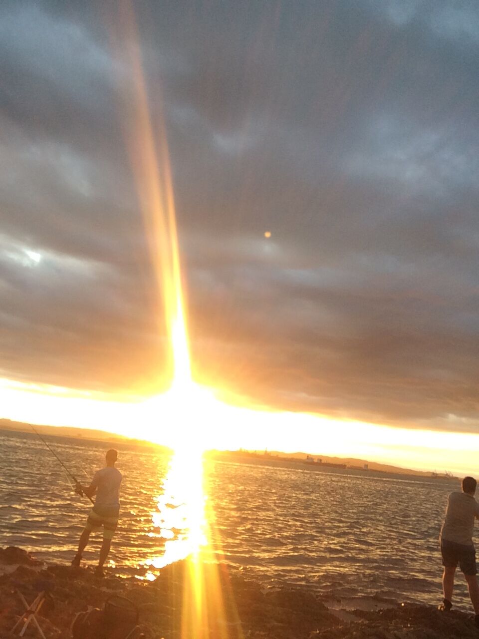 A sunset over a body of water with two people fishing.