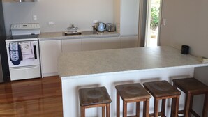 A modern kitchen with a central island, wooden stools, a built-in oven, and a sink. - Come and Relax @ Rose's Retreat (with WIFI) (Whangarei Heads)